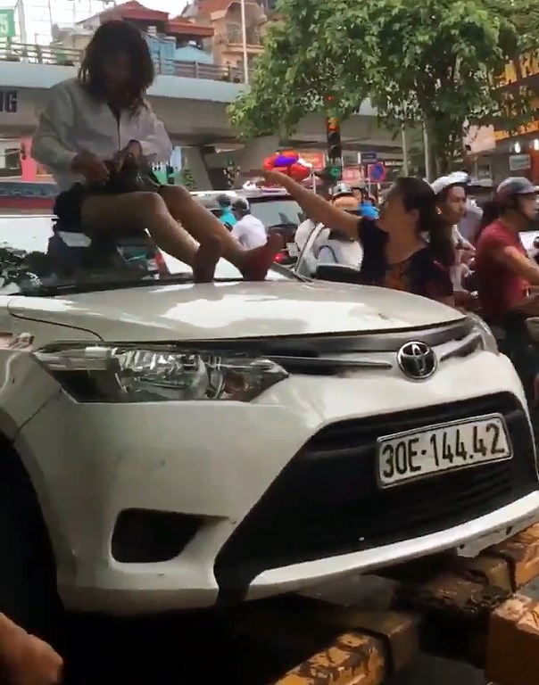 Mặc cho người dân khuyên can, nữ tài xế taxi ngồi trên nóc ô tô, cản trở lực lượng chức năng làm nhiệm vụ.